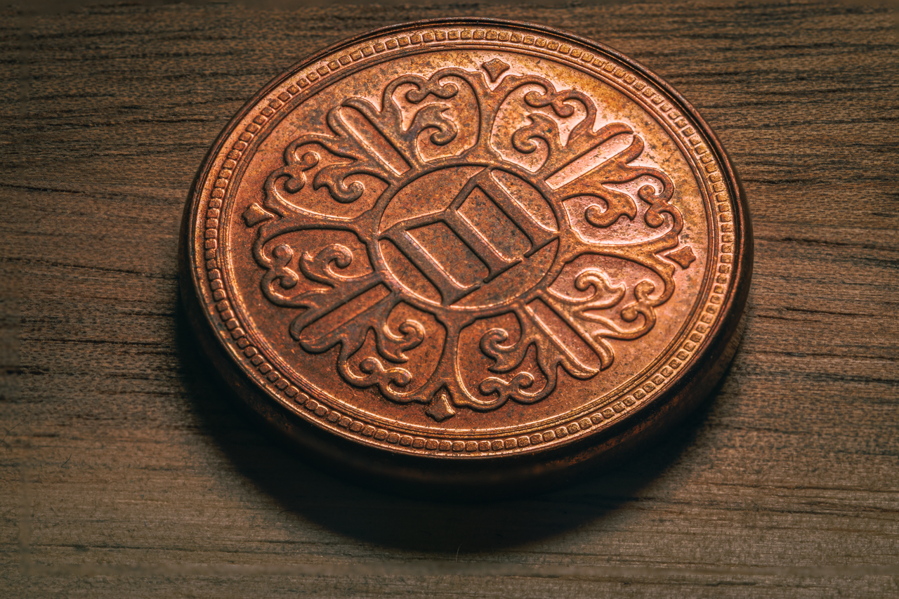 Close-up of an engraved copper coin featuring an intricate mythological design on a wooden surface.
